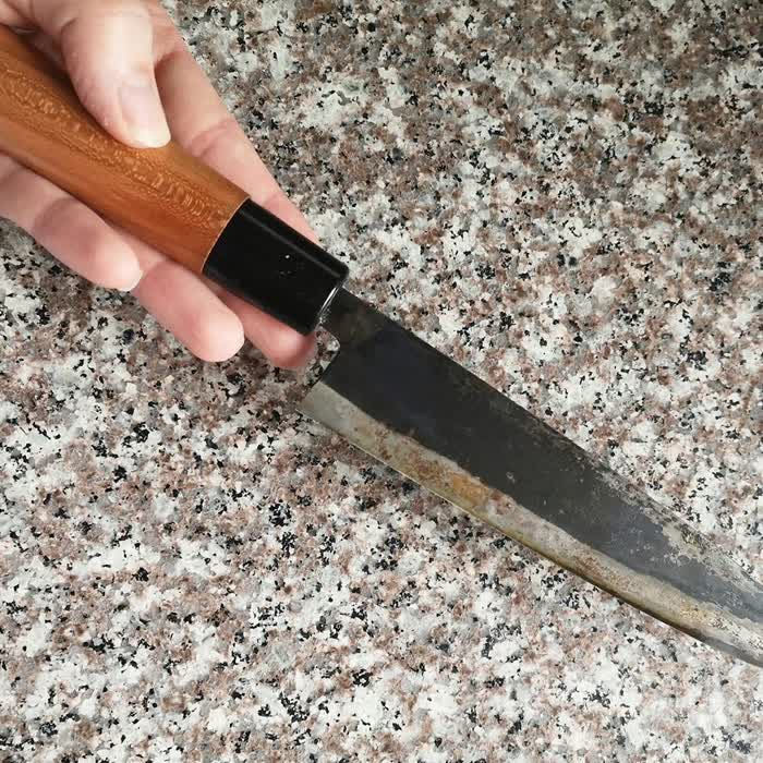 A chef's knife with a badly worn edge on a granite countertop